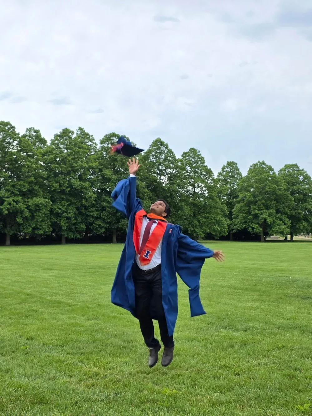 Saptarshi Joshi in a graduation gown, jumping to catch his cap on a lawn